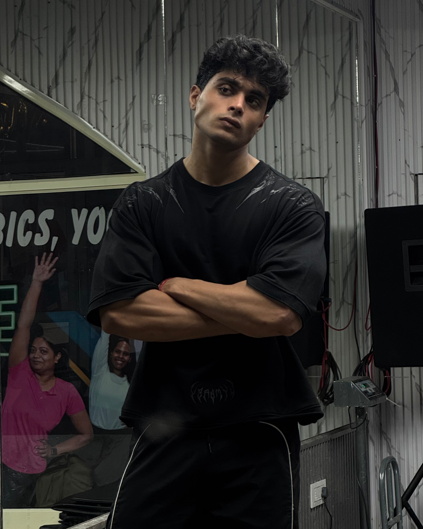Man in black outfit standing with arms crossed against a dark background