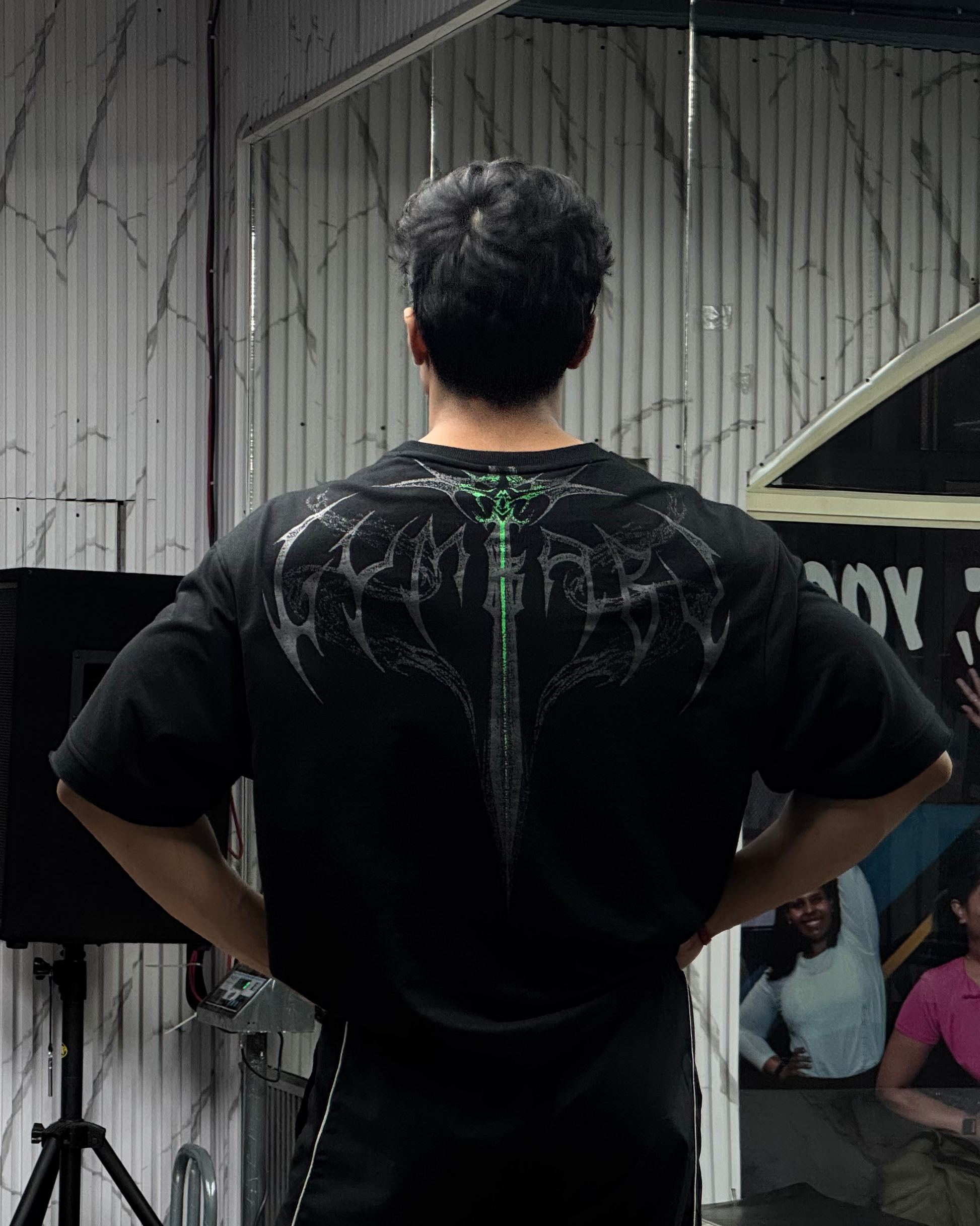 Person wearing a black t-shirt with a unique design, standing in front of a mirror.